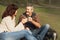 Middle-aged couple sitting on the grass in park and drinking tea.