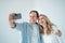 Middle aged couple standing embracing and taking selfie with smartphone