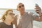 Middle-aged couple takes a selfie on the beach during a vacation - Happy elderly couple having fun playing with technology -