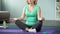 Middle-aged housewife sitting on yoga mat and meditating home, healthy lifestyle