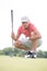 Middle-aged man aiming ball while crouching on golf course