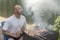 middle-aged man enjoys cooking meat on the grill. leisure, food, people and holidays concept - happy young man cooking meat on bar