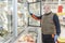 A middle-aged man in a medical mask and gloves chooses frozen foods in a supermarket refrigerator. Healthy eating during the