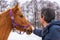 Middle-aged man patting horse at ranch in snowy day. Winter weekend at farm, trip to countryside. Healthy lifestyle, active