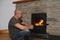 Middle-aged man sits near a hot burning fireplace and looks thoughtfully at the fire, concept of winter relaxation