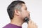 A middle aged man using a cordless trimmer to shape and trim his beard and sideburns. Facial care and grooming. Side view candid
