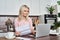 Middle aged mature woman holding paper bill or letter using laptop at home.