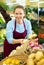 Middle-aged saleswoman putting onions on food stall in greengrocery