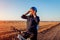 Middle-aged woman bicyclist taking on helmet in autumn field at sunset. Senior sportswoman enjoying hobby.