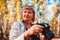 Middle-aged woman checking images on camera in autumn forest. Senior woman walking and enjoying hobby