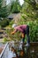 Middle aged woman clearing storm debris blocking a downspout drain to release rainwater flooding from a flat carport roof