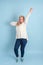 Middle-aged woman dancing listening to music in wireless headphones on a blue background, vertical photo