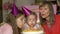 Middle aged woman and her granddaughters in party hats giving cake and blowing candles