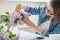 Middle-aged woman making bouquet of lilac branches, close-up female arranging flowers bunch in vase