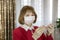 A middle-aged woman in a medical mask, looking at an electronic thermometer in a room of an apartment building, protection from vi