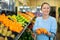 Middle-aged woman purchaser buying fresh tangerines in grocery store