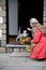 A middle-aged woman in a red cloak with a net of orange pumpkins opens the door