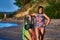 A middle aged woman with red hair is standing on a sandy beach and holding a surfboard.