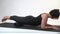 A middle-aged woman with saggy skin on a gymnastic mat with myofascial roller does an exercise on her hips on a white