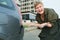 Middle-aged woman with a short haircut is shocked by the bumper damage on her car