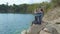 Middle-aged woman sits on elevated rocky shore and takes video on her smartphone. Hiking tourism concept