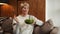 Middle-aged woman is sitting and resting at home on the couch, eating a green salad. A woman eating healthy food.