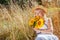 Middle-aged woman smells bouquet of yellow sunflowers relaxing in summer field with high grass outdoors.