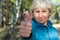 A middle-aged woman smiles and shows a thumbs up. Walk in the park on a bright sunny day.