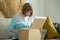 Middle aged woman unpacking cardboard box, sitting on sofa at home. Senior woman hold open cardboard box sit on sofa in