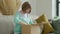 Middle aged woman unpacking cardboard box, sitting on sofa at home. Senior woman hold open cardboard box sit on sofa in