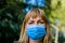 Middle aged woman wearing blue virus mouth nose mask nice backlight sun bokeh in background closeup face portrait People