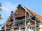 Middle aged workman standing on scaffolding fitting roof tiles to residential cottage