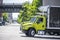 Middle duty day cab big rig semi trucks with refrigerated box trailers standing on the warehouse parking lot on the city street