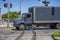 Middle duty day cab gray rig semi truck with box trailer transporting cargo running on the city street crossroad with traffic