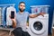 Middle east man with beard showing smartphone screen and washing machine looking at the camera blowing a kiss being lovely and