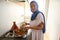 Middle Eastern woman housewife in hijab and authentic dress, putting some chickpeas in a tajine dish with vegetables