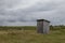 In the middle of the meadow stands a rustic public toilet made of wooden planks