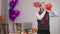 Middle shot of adult Caucasian stylish man blowing heart shape balloon standing at Valentine's dinner table indoors