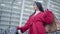 Middle shot bottom view of elegant Caucasian brunette girl in red coat standing outdoors with shopping bags. Young