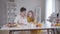 Middle shot of Caucasian woman and girl reading recipe at the table with ingredients for pancakes. Confident grandmother