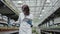 Middle shot of confident female biologist looking at seedlings or flowers in greenhouse and taking notes in tablet