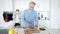 Middle shot of handsome senior man slicing cucumber for healthful salad as blurred cheerful woman talking on the phone