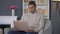 Middle shot portrait of concentrated young African American man sitting on armchair typing on laptop keyboard. Focused