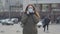 Middle shot of young brunette woman standing on city street and putting on protective mask. Anxious woman protecting