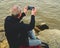 Midle aged man sitting on the shore of the lake. Solitude mature man taking selfie picture on the bank. Concept o