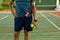 Midsection of biracial senior man holding balls and racket with hand on hip standing at tennis court