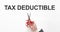 Midsection of businessman cutting the word TAX DEDUCTIBLE on paper with scissors over gray background