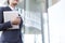 Midsection of businesswoman holding tablet PC by glass wall