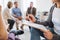 A midsection of counselor with clipboard talking to a client during group therapy.