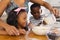 Midsection of multiracial mother pouring milk in bowl while standing with children in kitchen